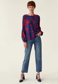 Blomsterbluse i blå og rød, lange ærmer, rund hals; parret med lyseblå lige ben jeans og marineblå højhælede sko.