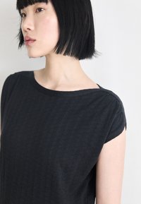 Top preto texturizado com decote redondo e mangas curtas, apresentando um padrão subtil por toda a peça. Design simples e casual.