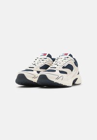 Adidași bej și bleumarin cu un superior din plasă și material sintetic, talpă din cauciuc, șireturi groase și un design cu profil redus, cu accente de logo.