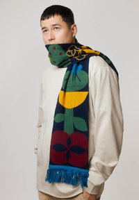 Dziany szalik z kolorowymi kwiatowymi wzorami w zieleni, żółci, czerwieni i niebieskim, z frędzlami na końcach i ciemnogranatowym tle.