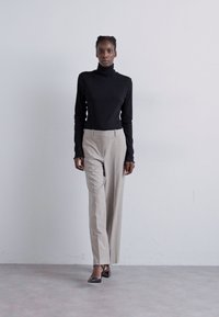 Melnā turtleneck blūze ar teksturētu detaļu, apvienota ar bēšiem pielāgotiem biksēm un melniem asiem zābakiem. Vienkāršs, mūsdienīgs dizains ar slaidu piegriezumu.