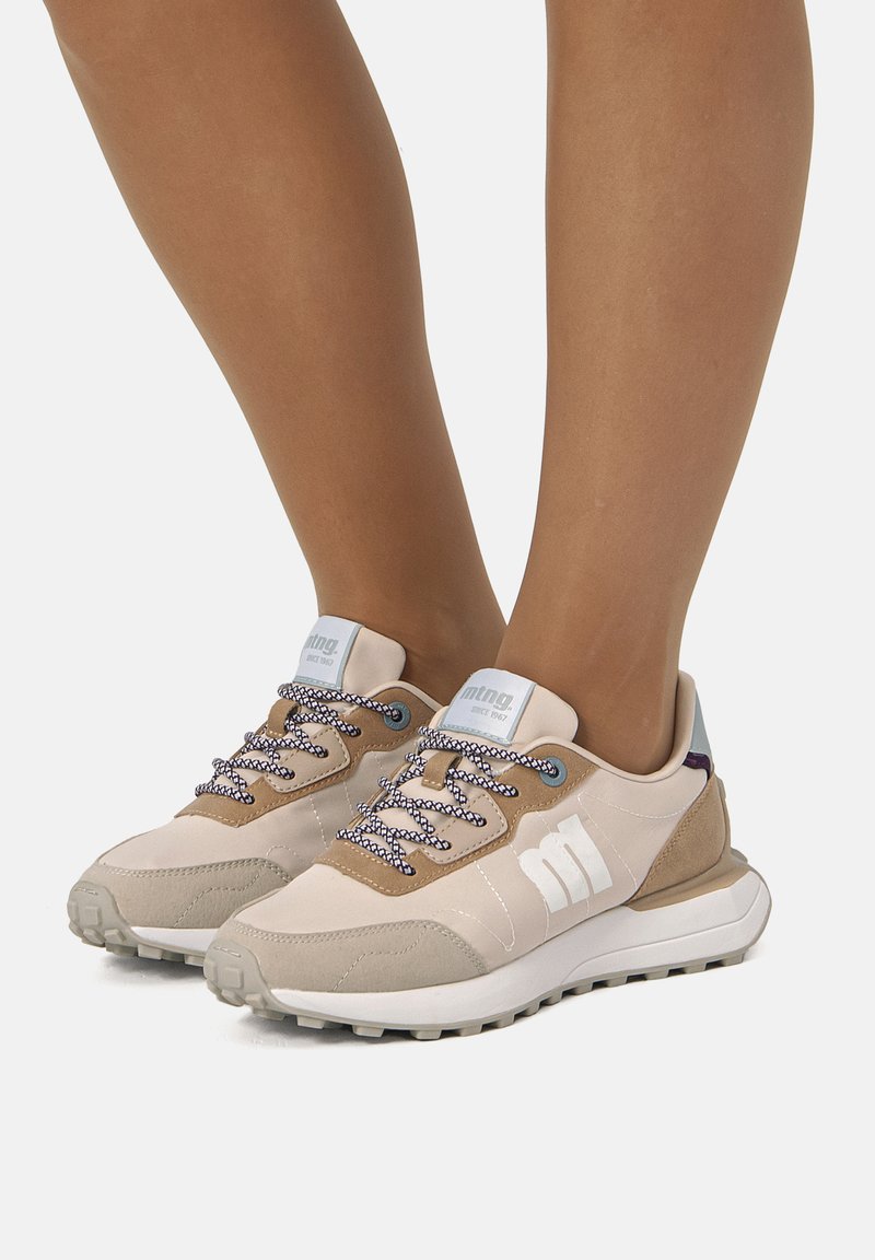 Beige Sportschuhe mit Obermaterial aus Wildleder und Mesh, gemusterten Schnürsenkeln, strukturiertem Mittelsohlenbereich und ausgeprägter Gummiaußensohle. Markenlogo seitlich sichtbar.