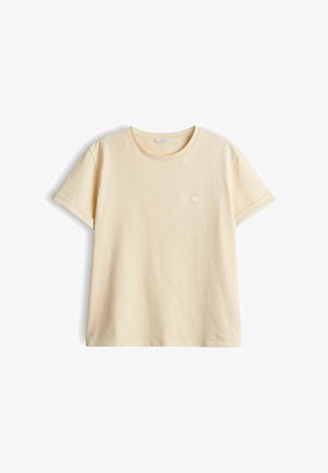 Crème kleurige katoenen T-shirt met korte mouwen, ronde hals, opgerolde manchetten en een klein geborduurd hart op de linkerborst.