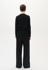 Schwarzer Pullover mit langen Ärmeln und weite Hosen, beide aus einem glatten Strickmaterial, von hinten vor einem neutralen Hintergrund betrachtet.