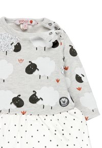 Vestido de algodón gris con mangas largas, que presenta estampados de ovejas en blanco y negro, detalles en naranja y una falda blanca con lunares, con una etiqueta.