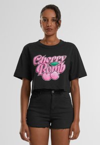 Crni skraćeni majica od pamuka s sjajnim ružičastim grafičkim prikazom "Cherry Bomb" koji sadrži trešnje i zeleni list u sredini.