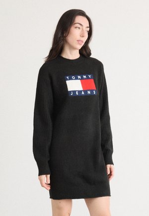 Abito lungo nero a maglia con maniche a coste, presenta una patch rettangolare colorata con la scritta "TOMMY JEANS" in bianco e blu.