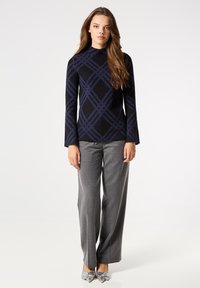 Suéter de color azul marino con un patrón y textura acanalada, combinado con pantalones de pierna ancha grises y zapatos de punta plateados. Mangas largas y cuello alto.