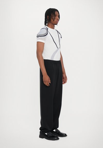 Weißes Kurzarmhemd mit grauen Akzenten und Mesh-Details, kombiniert mit lockeren schwarzen Hosen und schwarzen Schuhen. Minimalistisches Design, entspannter Schnitt.
