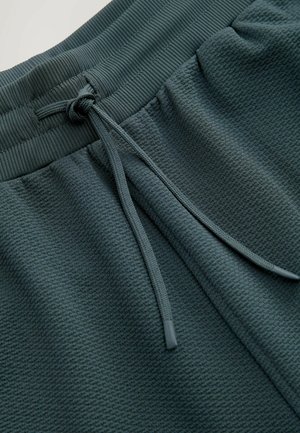 Mørkegrønne textured sweatpants med ribbet talje og snørrebånd. Stoffet har et subtilt mønster for ekstra detalje.