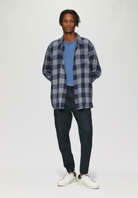 Gegatairede overhemd in marineblauw en grijs, gelaagd over een lichtblauwe T-shirt. Zwarte cargobroek, witte sneakers met marineblauwe accenten. Casual fit.