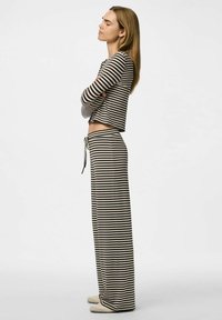 Ensemble de loungewear rayé en noir et crème ; haut court à manches longues avec un col rond, associé à un pantalon ample à taille haute.