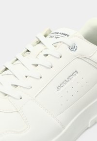 Close-up of white Jack & Jones sneaker with white laces, perforated side panel, and brand name embossed on the upper.
