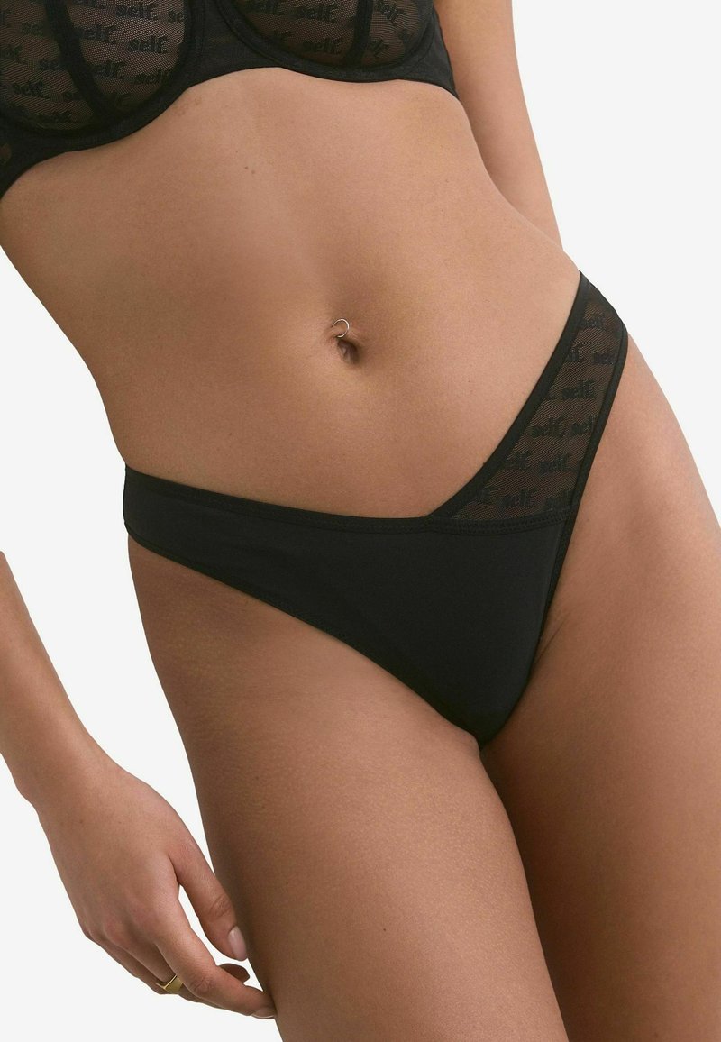 Perizoma nero con dettagli in rete trasparente nella parte anteriore, design a vita bassa e copertura minima. Presenta una texture di tessuto liscia.