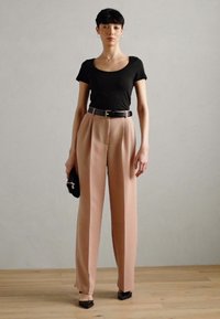 Camiseta negra ajustada, pantalones de pierna ancha en rosa claro de cintura alta, cinturón negro y pequeño bolso de mano negro. Tejido suave, diseño estructurado.