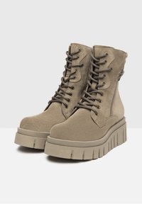 Bottines en suède beige à lacets, avec fermeture éclair sur le côté et semelle plateforme épaisse présentant des rainures horizontales.