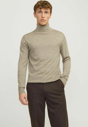 Suéter beige de cuello alto con mangas largas, hecho de una tela suave y texturizada. Diseño ajustado combinado con pantalones oscuros.
