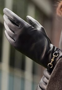 Schwarzer Lederhandschuh mit glatter Textur, enganliegendem Design und einem goldfarbenen Hardware-Detail am Handgelenk.
