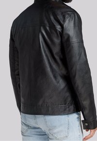 Giubbotto di pelle nera con una texture liscia, schiena senza dettagli e polsini con bottoni a pressione, abbinato a pantaloni in denim azzurro chiaro.
