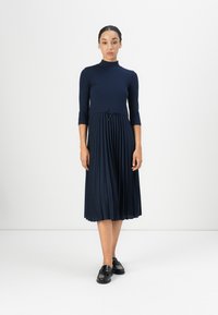 Navy blue dress with a ribbed bodice, three-quarter sleeves, and a pleated skirt. Features a drawstring at the waist and falls below the knee.