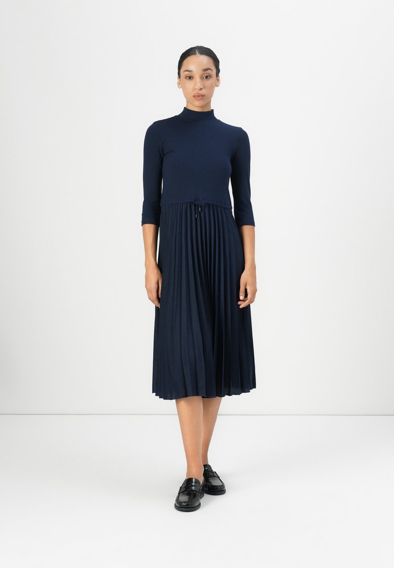 Navy blue dress with a ribbed bodice, three-quarter sleeves, and a pleated skirt. Features a drawstring at the waist and falls below the knee.