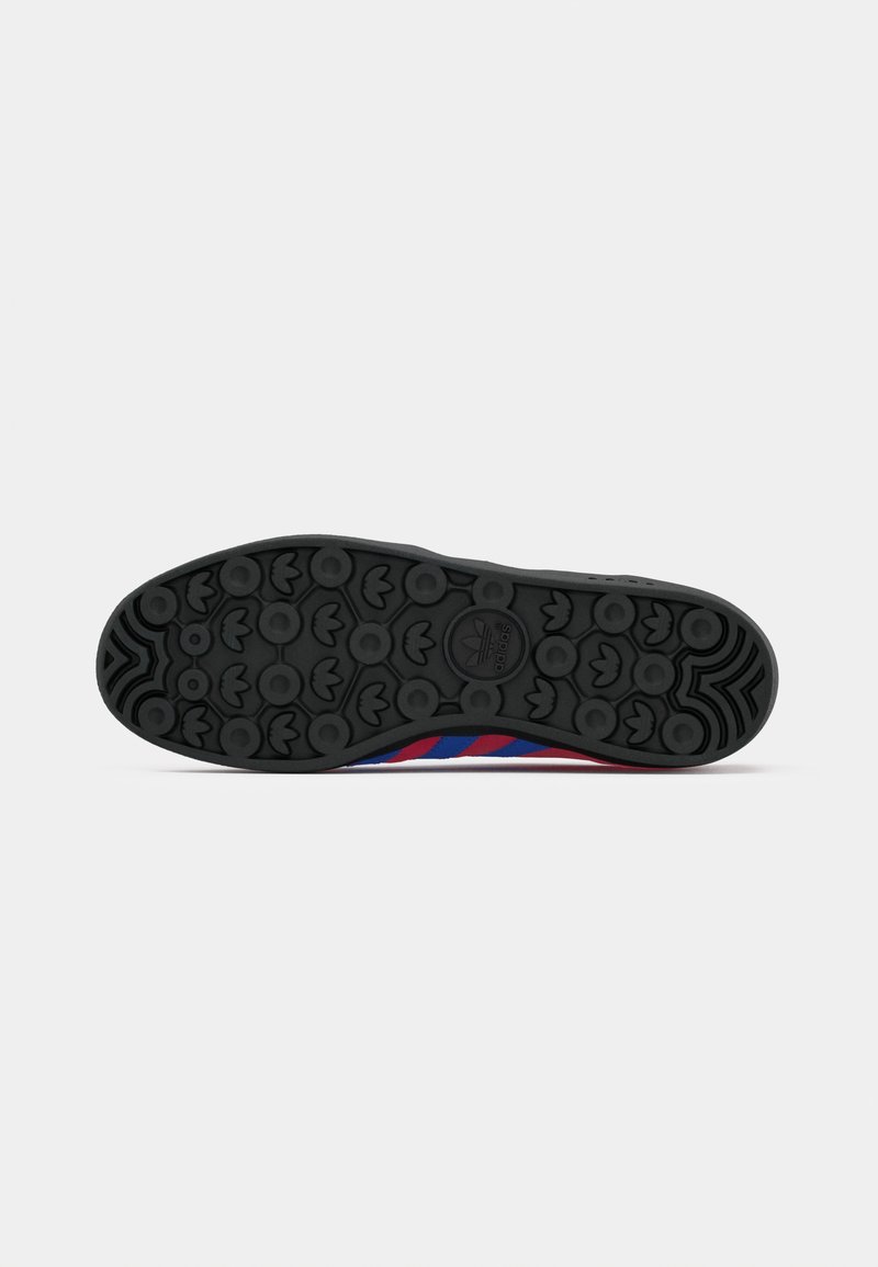 Semelle de chaussure de sport noire en caoutchouc avec motifs de traction circulaires, présentant des accents rouges et bleus sur les côtés et un détail de logo central.