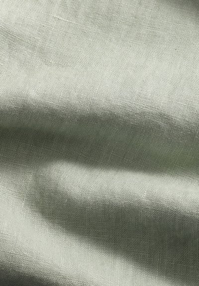 Gedämpfter grüner Leinenstoff mit einer strukturierten Webart, der sanfte Falten und einen subtilen Glanz zeigt und seine leichte und atmungsaktive Qualität betont.