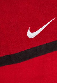 Asciugamano rosso realizzato in tessuto testurizzato, con il logo Nike in bianco e una banda nera lungo il bordo inferiore.