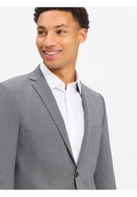 Grijze op maat gemaakte blazer met een fijne textuur, enkele knoopsluiting en een borstzak. Gecombineerd met een frisse witte overhemd.