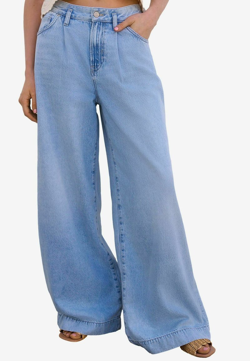 Jeans de pierna ancha de color azul claro con cintura alta, confeccionados en denim. Incluyen bolsillos frontales y un ligero desgaste.