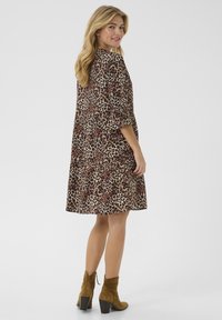 Luipaardprint jurk met driekwart mouwen, vloeiende silhoutte en een zoomlijn boven de knie. Bruine suède enkellaarsjes met een blokhak.