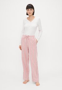 White long-sleeve top with a buttoned placket, paired with red and white striped pajama pants featuring an elastic waistband and drawstring.