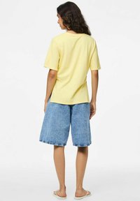 T-shirt di cotone gialla a maniche corte, abbinata a pantaloni Bermuda in denim blu. Il tessuto ha una texture liscia e una vestibilità casual.