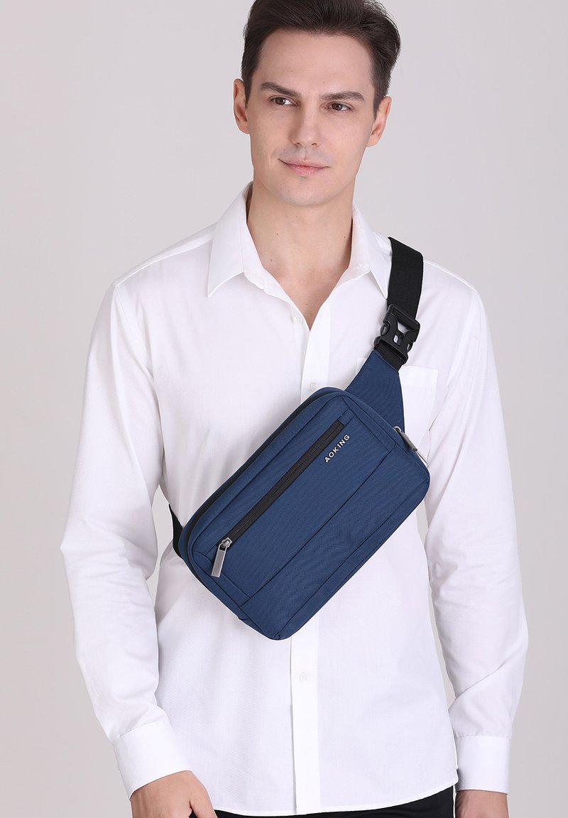 Borsa a tracolla blu navy realizzata in tessuto testurizzato, con un compartimento con zip, tracolla nera regolabile e un branding minimalista.
