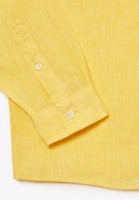 Camisa de lino amarilla de manga larga, con puños abotonados y un sutil patrón de tela texturizada.