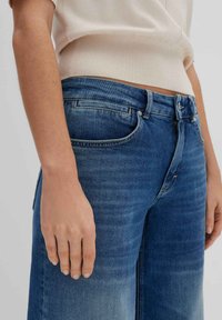 Jeans en denim bleu avec une taille mi-haute, design classique à cinq poches et une finition légèrement délavée. Vue en gros plan, montrant la texture et l'ajustement.