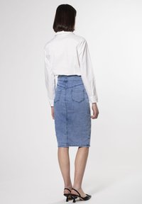 Jupe en denim bleu clair, avec une taille haute, des poches arrière et une silhouette droite. Associée à une chemise blanche à boutons.