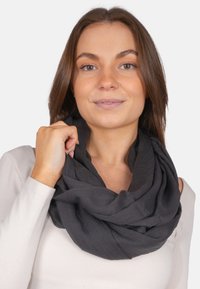 Black circular scarf made from lightweight fabric; features a soft, textured surface with gentle draping and folded layers.