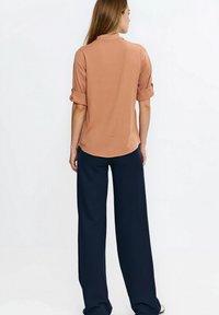 Brązowa koszula z krótkim rękawem i podwiniętymi mankietami, w połączeniu z luźnymi, granatowymi spodniami o szerokich nogawkach. Gładka tkanina o luźnym kroju.