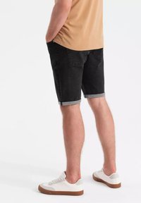 Shorts de mezclilla negros con dobladillos enrollados, presentando un diseño clásico de cinco bolsillos. Combinados con zapatillas blancas, exhibiendo un aspecto limpio y casual.