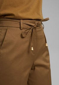 Hnědé kalhoty s páskem na stažení, zdobené zlatými detaily a hladkým povrchem. Design obsahuje přední zřasení a čisté zakončení.