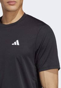 Svart atletisk t-shirt med texturerad tyg, korta ärmar och en vit logotypdetalj på bröstet. Crew neck-design.