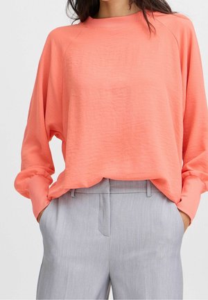 Sweatshirt surdimensionné corail avec col rond côtelé et manches longues, associé à un pantalon tailleur gris clair, présentant une texture lisse.