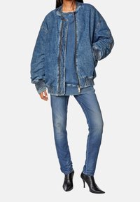 Oversized blue denim bomber jacket with ribbed cuffs and hem, paired with fitted blue jeans and black high-heeled boots.