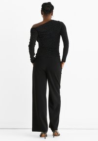Black off-shoulder top with ruched design, embellished with small silver dots, paired with high-waisted black trousers and strappy heels.