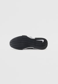 Crna sneaker potplat s teksturiranim, cik-cak uzorkom; ima bijeli Nike logotip i isječeni dio. Izrađen od izdržljive gumene materije.