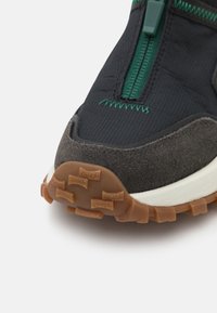 Black and gray hiking shoe featuring a textured upper, rubber outsole with grip, and green accents. Zip closure along the instep.