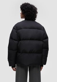 Czarna pikowana kurtka z wysokim kołnierzem, z ryflowanymi mankietami, noszona na szare, szerokie spodnie.