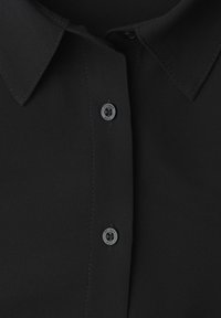 Sort bluse med klassisk krave, skjult knaplukning og matte sorte knapper med "Street Duo" indgraveret. Glat tekstur.