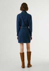 Denim dress in dark blue, fitted waist, shirt collar, long sleeves, and button cuffs. Knee-length with contrasting stitching. Brown suede knee-high boots.